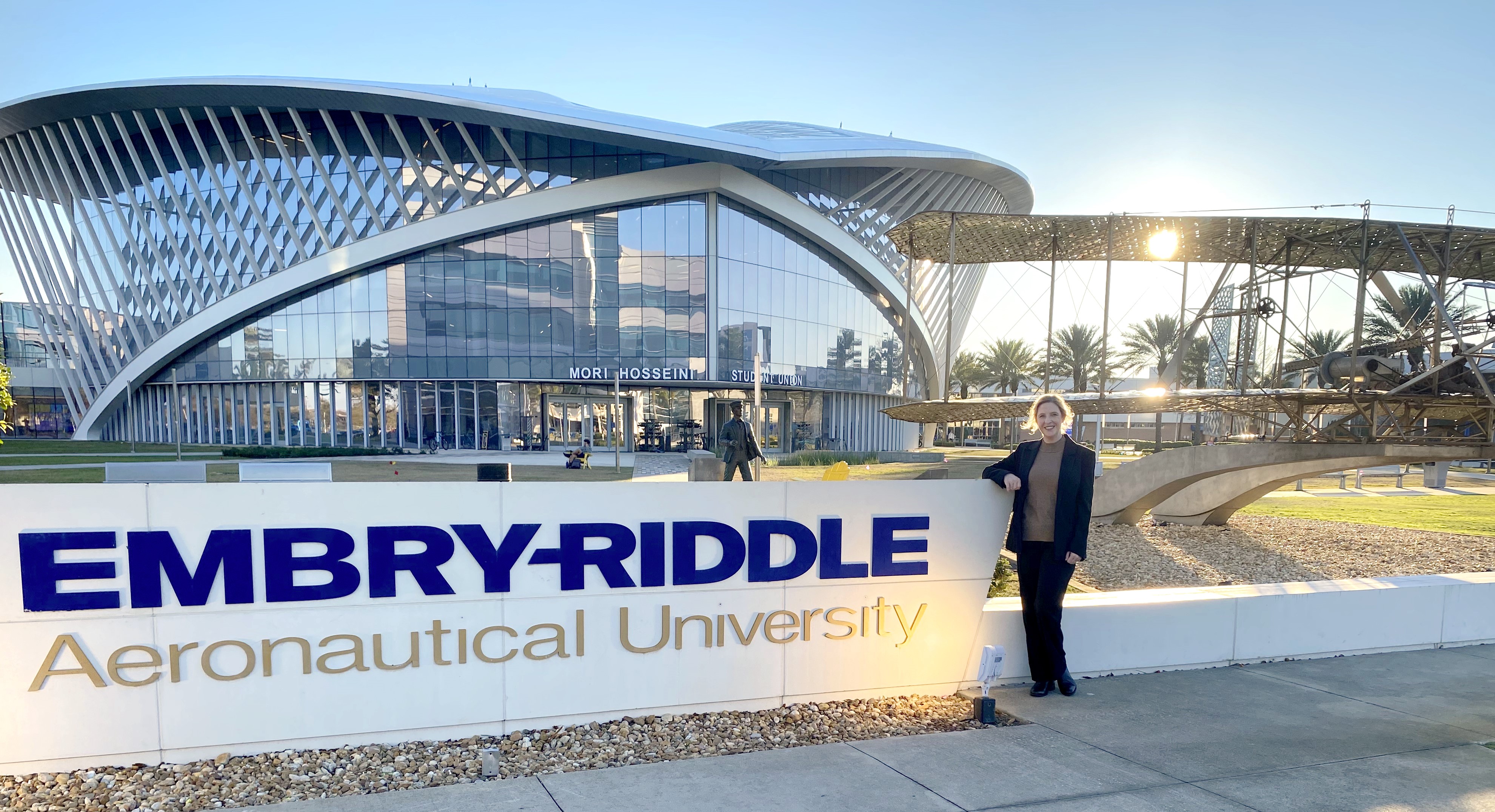 A woman in a blazer standing next to a sign that reads "Embry-Riddle Aeronautical University"